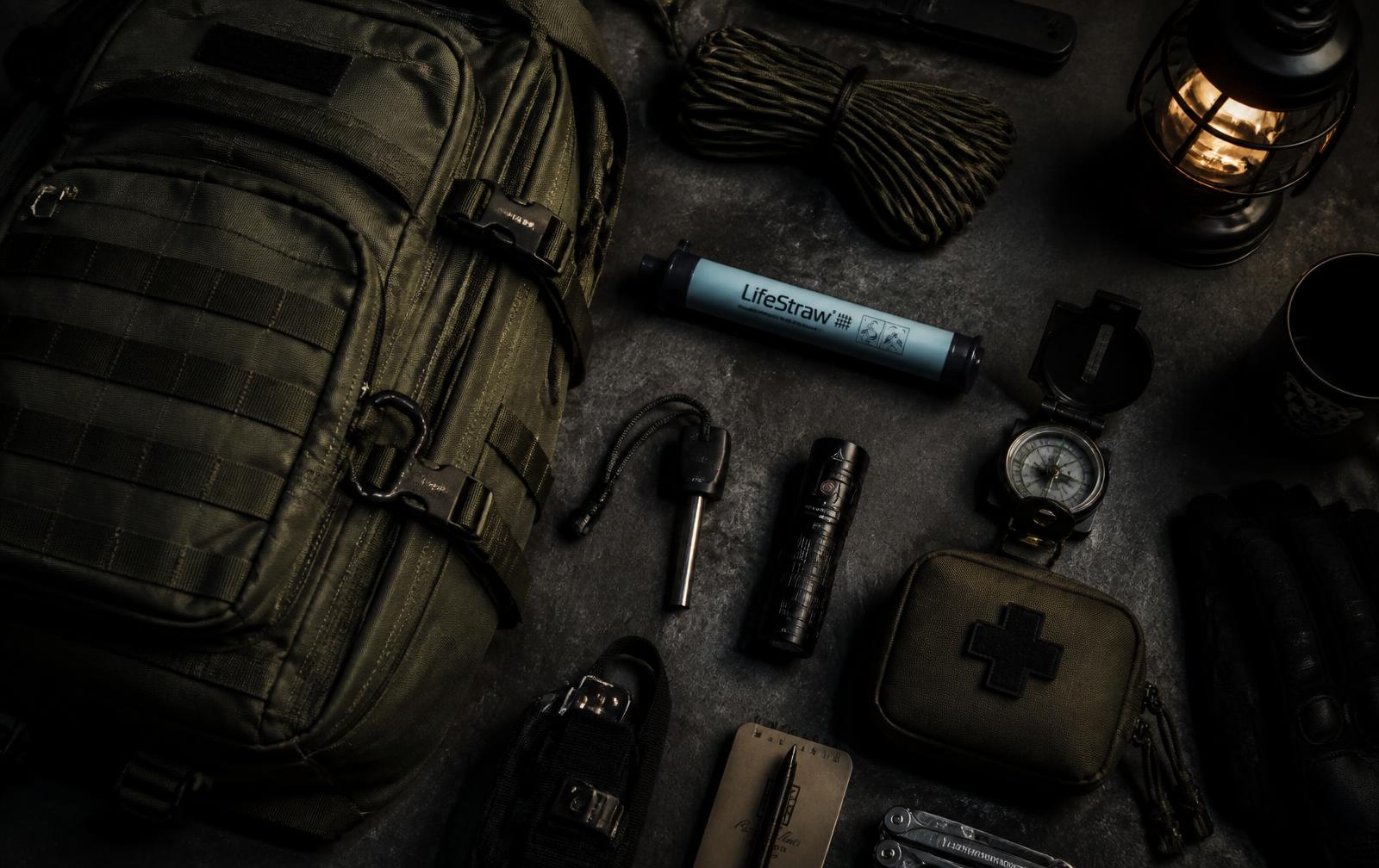 Prepping gear laid out: bug-out bag, water filter, ferro rod, torch and first aid pouch